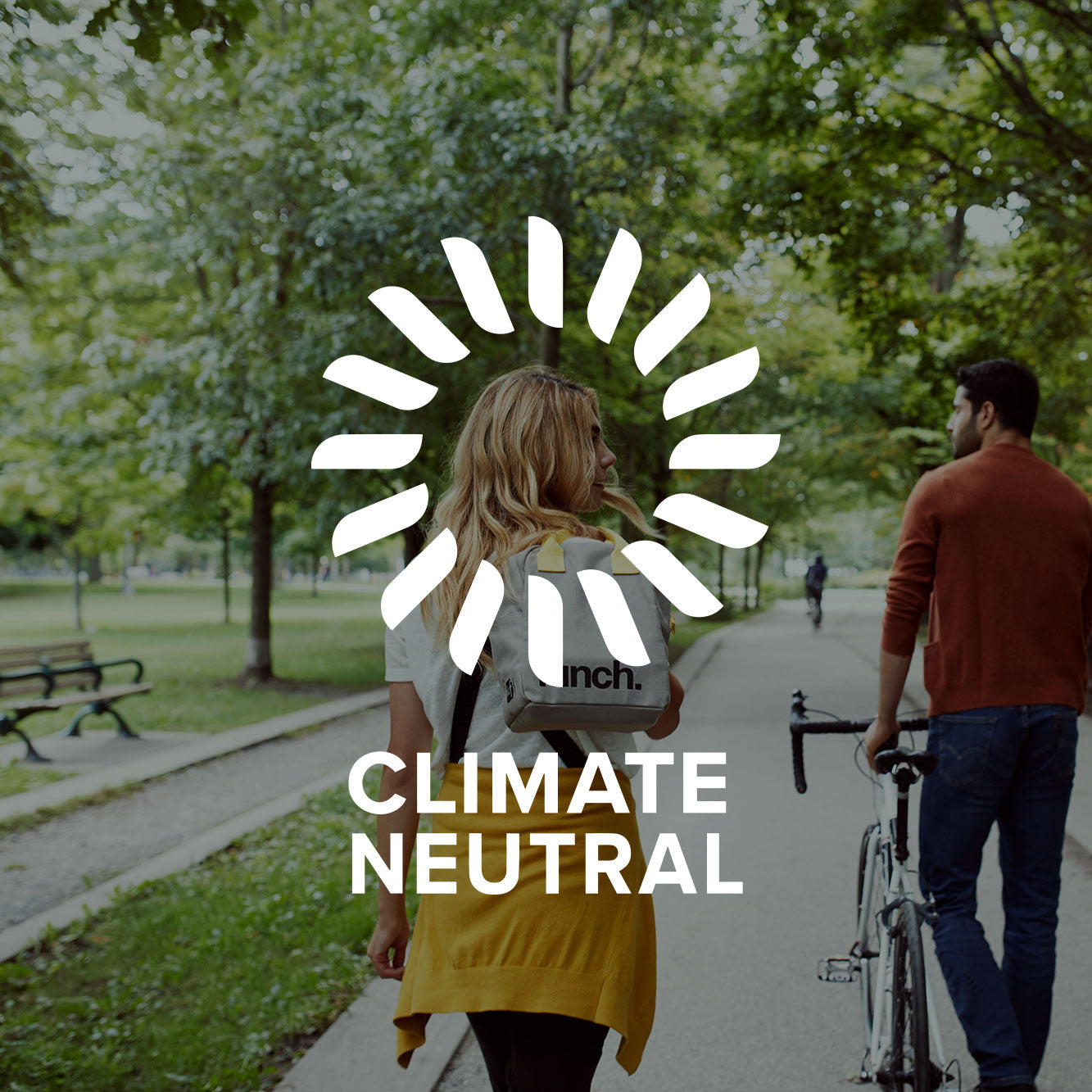 A woman walking in the park with white eco friendly lunch bag with printing of black text of the word "Lunch" on the image circle with text "climate neutral" representing Fluf's Climate Neutral Commitment to environmental efforts