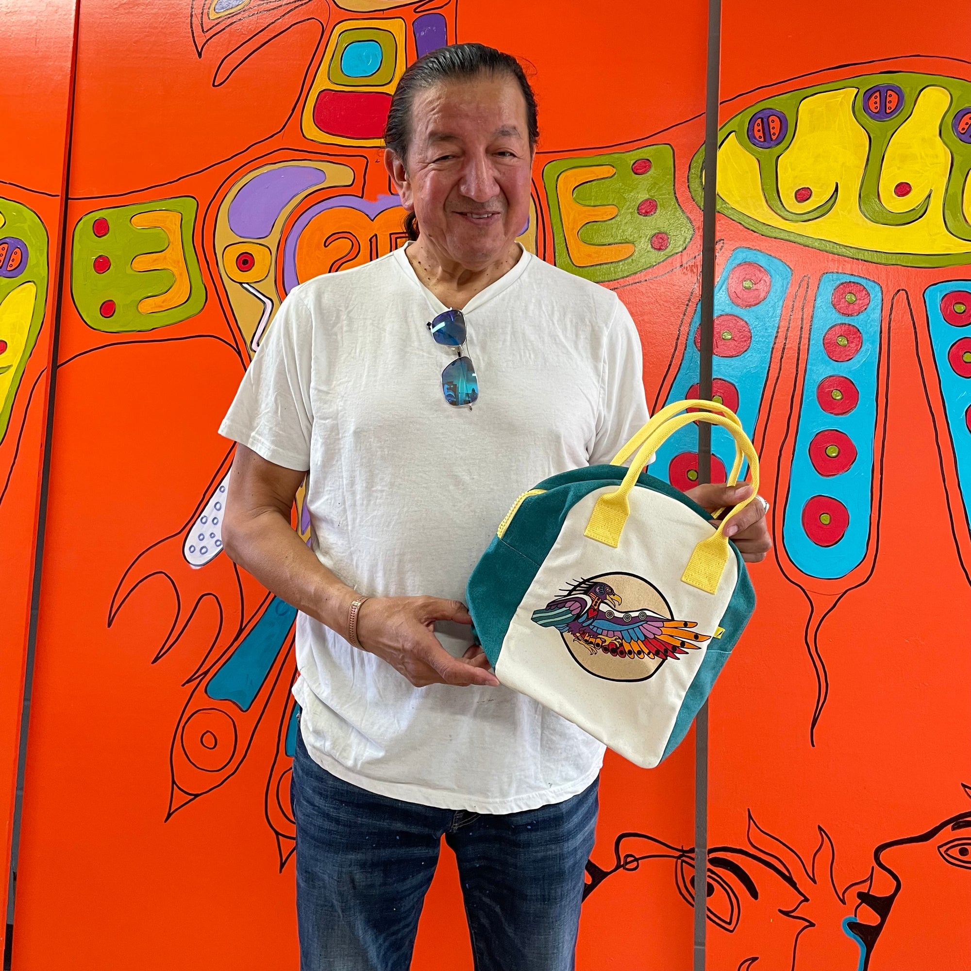 Photo of Philip Cote holding Fulf's lunch bag with eagle bright orange background art mural