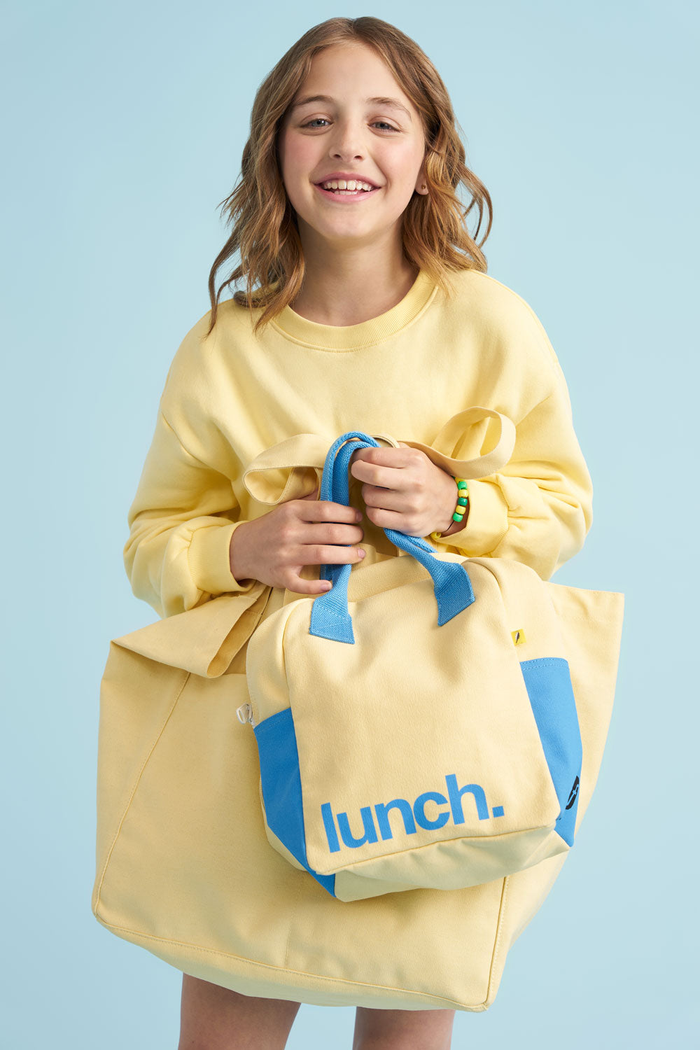 Girl holding a yellow lunch bag with blue accents against a light blue background
