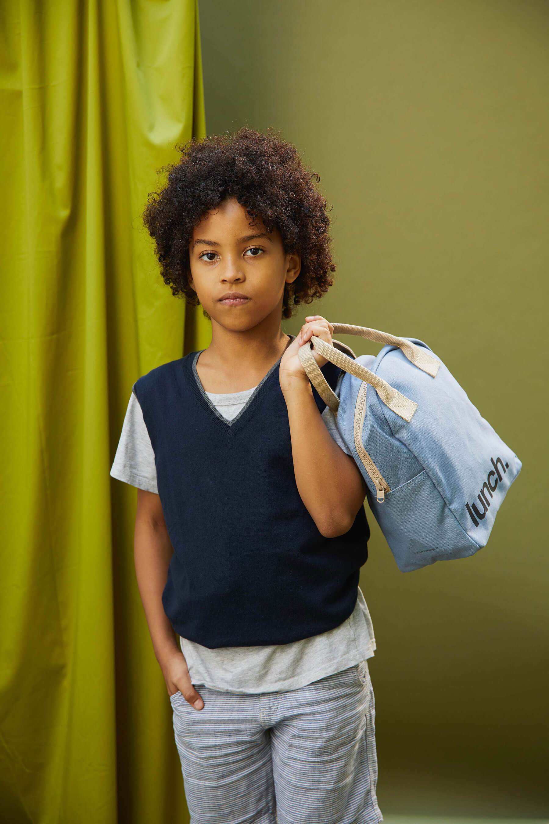 A boy holding a blue Zip Lunch Bag by Fluf