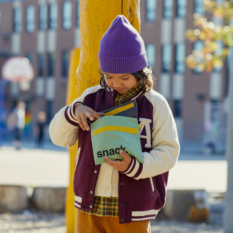 A boy holding a green reusable snack bag to demonstrate that it is food safe and suitable for children's use