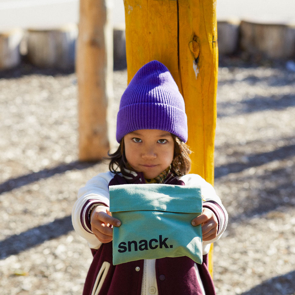 A boy holding a green reusable snack bag to demonstrate that it is food safe and suitable for children's use