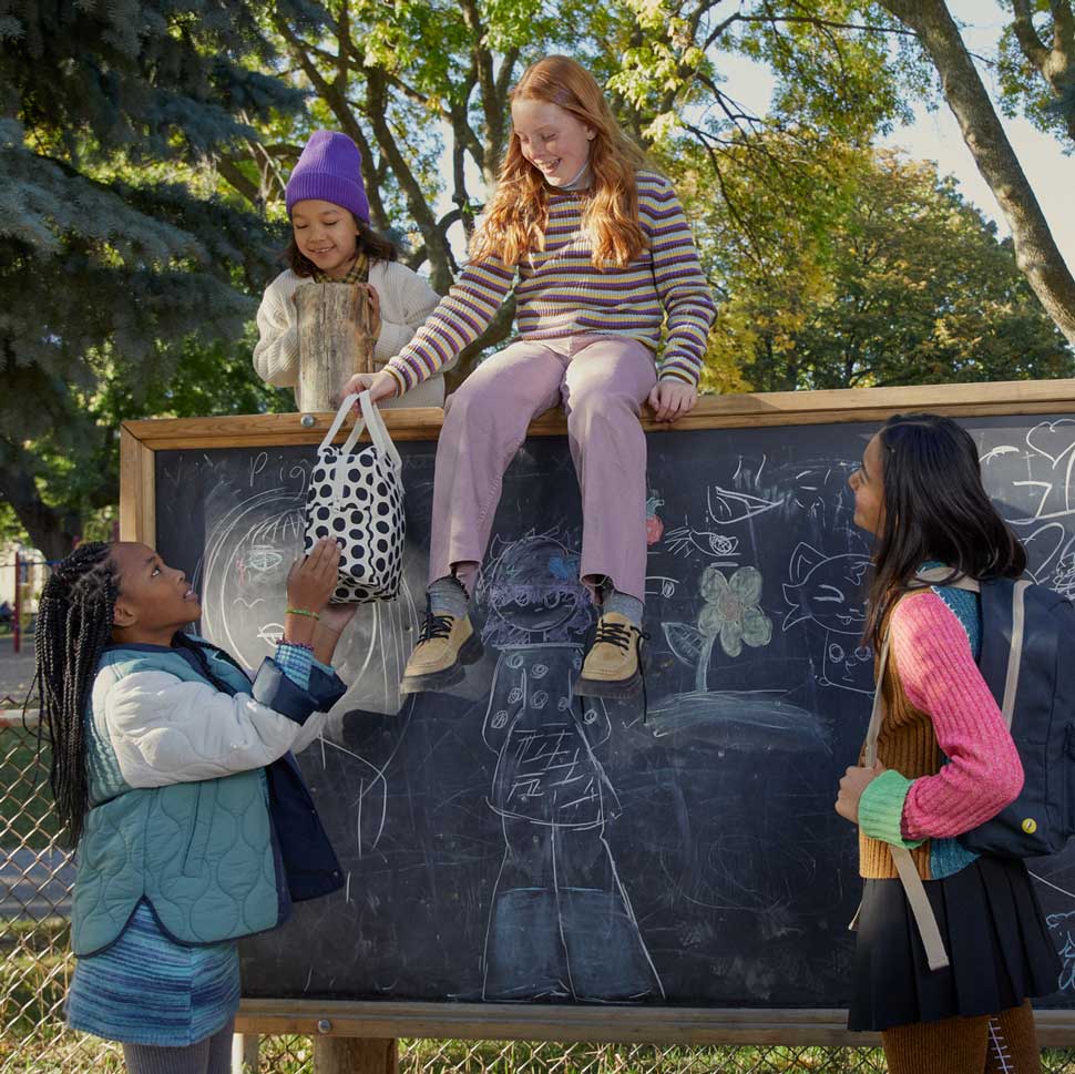 4 girls, one holding black polka dots lunch bag by Fluf to describe that the bags are good for kids and teens. 