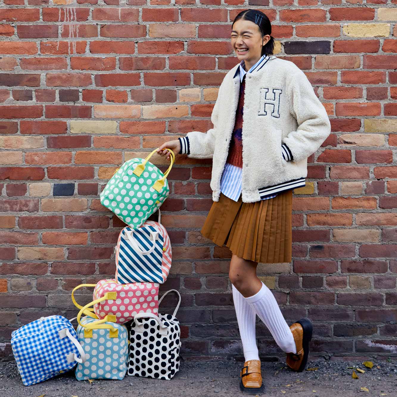 A teen girl standing near 6 stylish lunch bags designed for teenagers, kids and adults